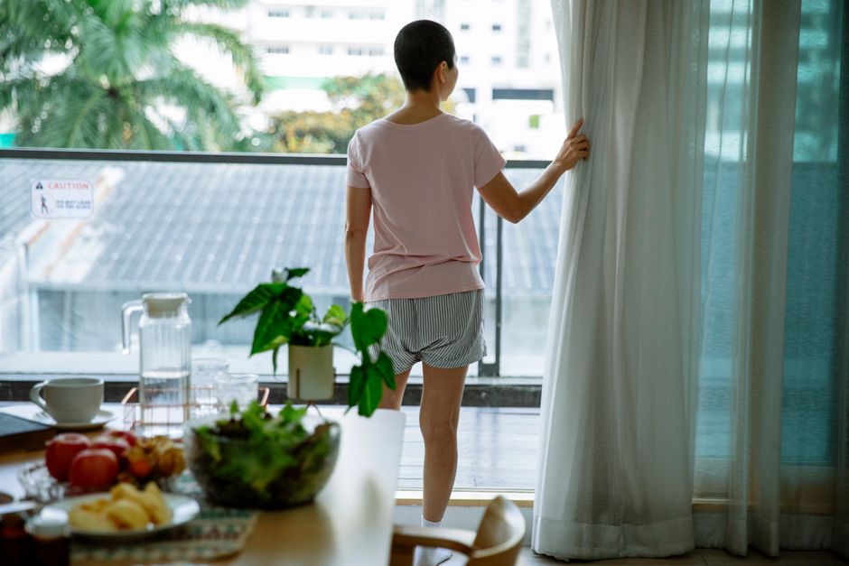 カーテンを開け朝日を浴びる女性